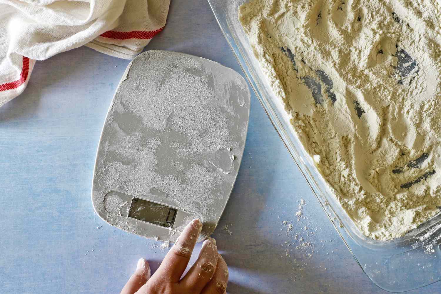 A touchscreen kitchen scale covered in flour with a dish of flour beside it