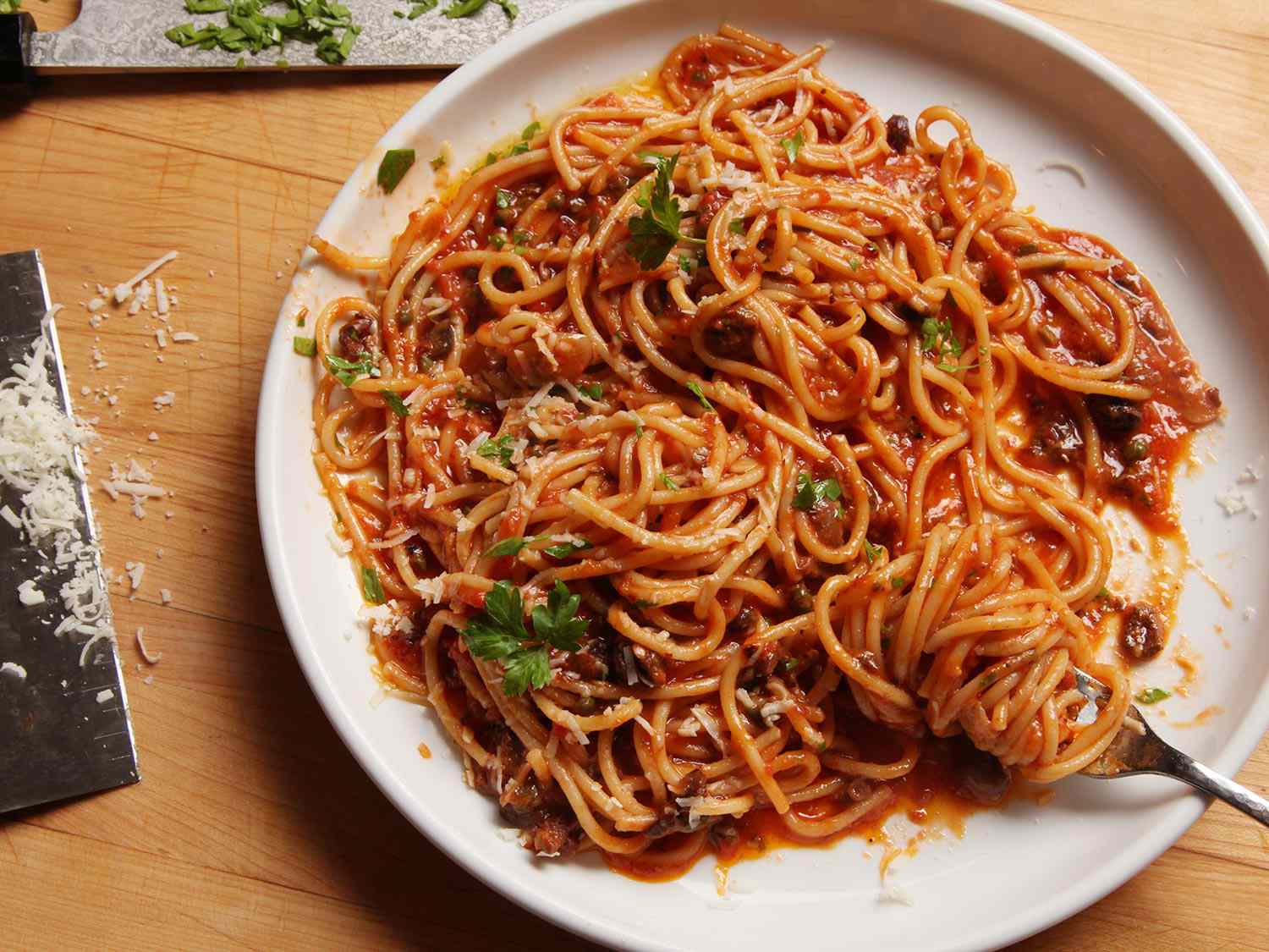 Pasta puttanesca, made with spaghetti, on a white plate.