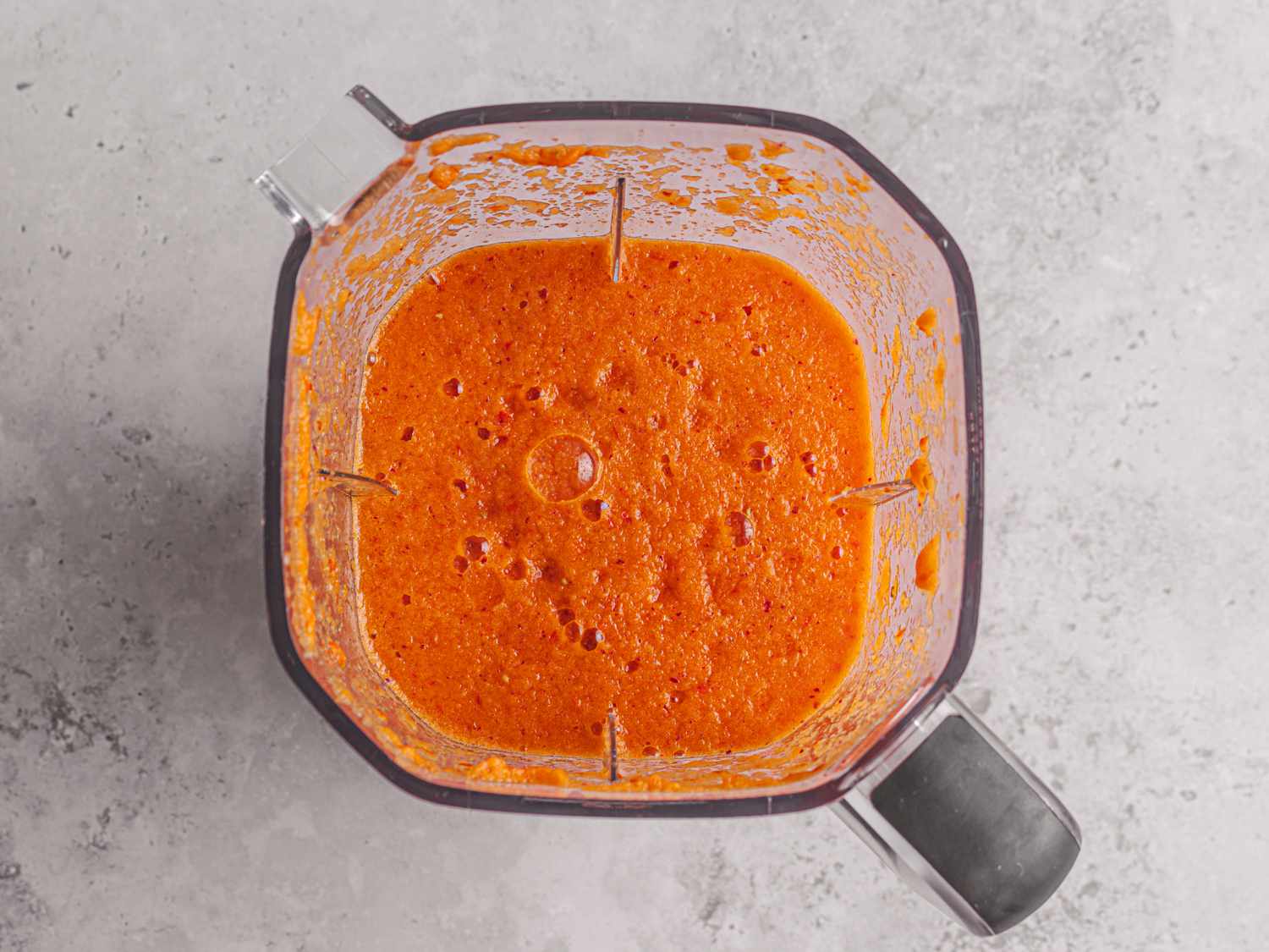 Overhead view of the puréed, bright orange ingredients for the stew base in the carafe of a blender