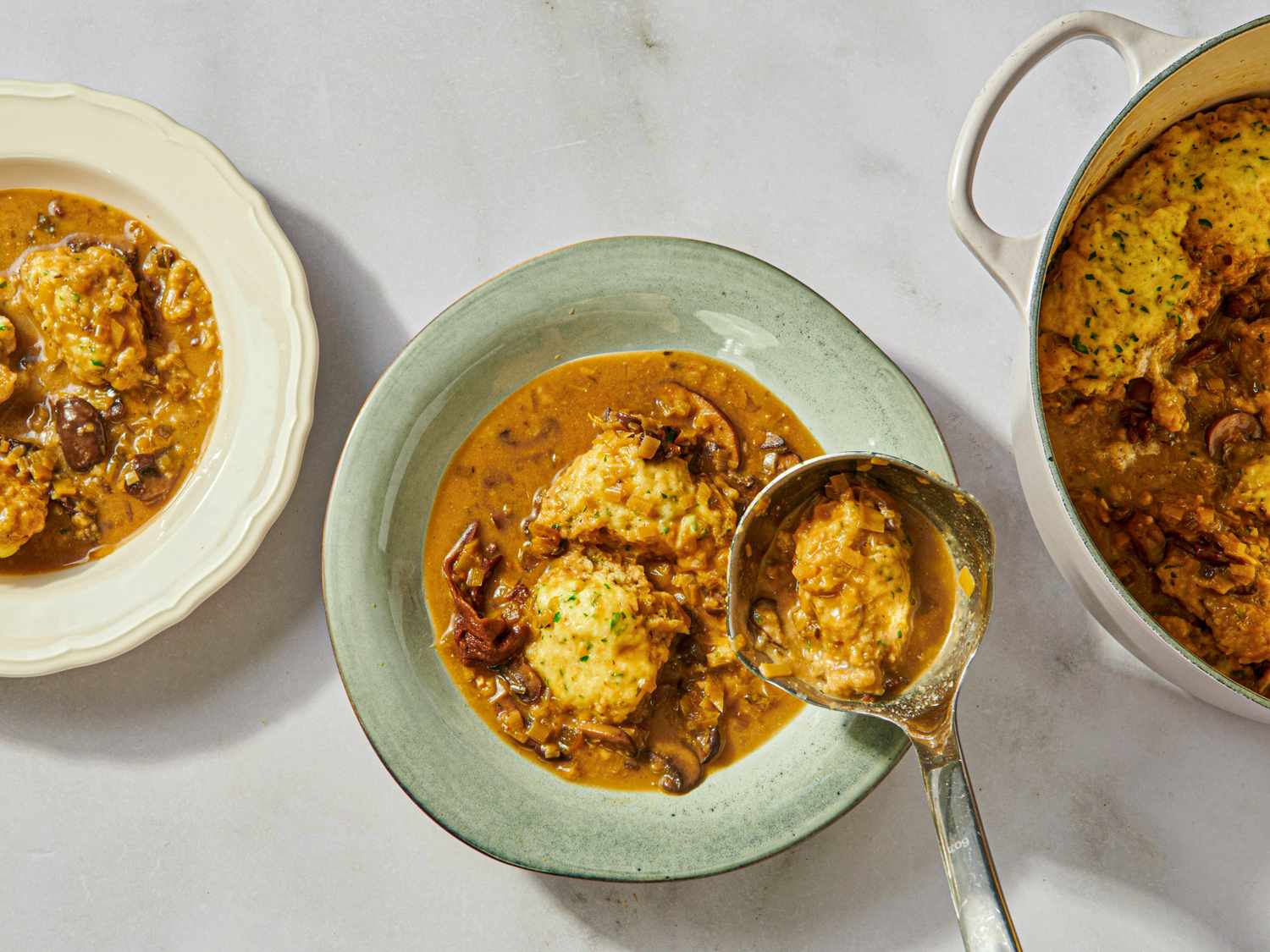 Bowls and a pot of mushroom and dumpling soup served with a ladle on a white table