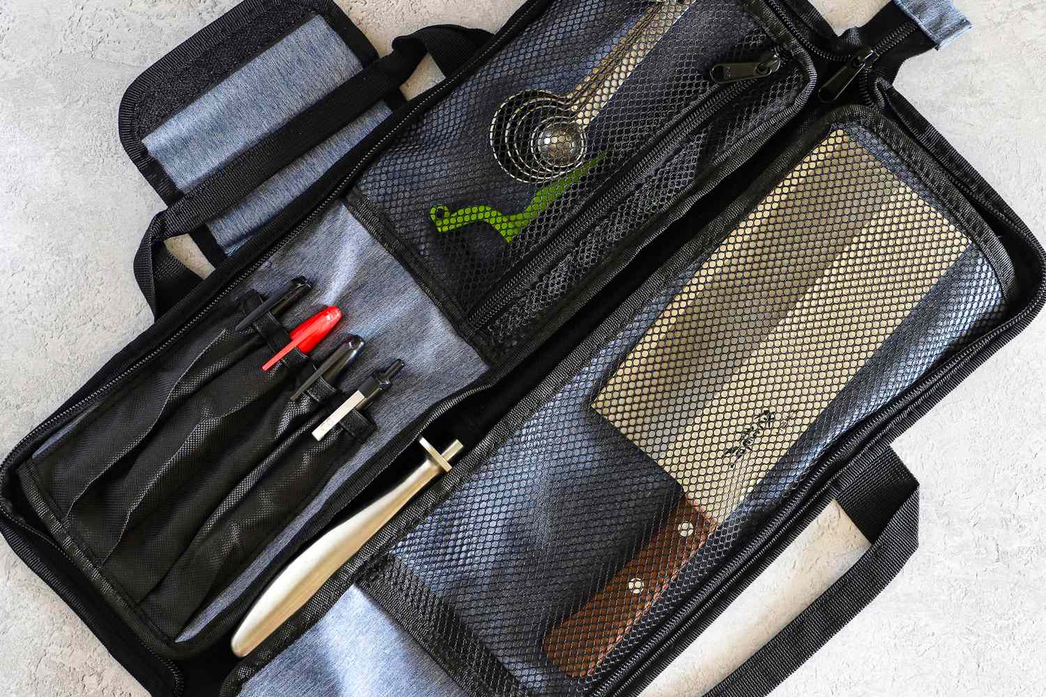 A culinary knife set and utensils stored in a black Asaya Chef Knife Roll Bag with compartments and mesh pockets