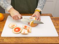 a person cutting the skin off of a grapefruit on the winco board