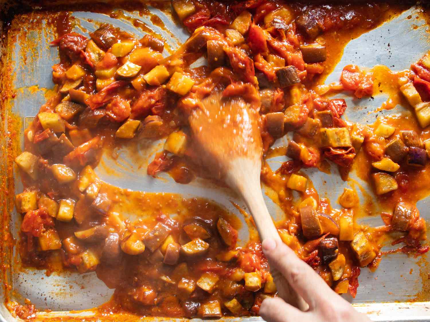 Stirring together roasted tomatoes and eggplants on a sheet pan