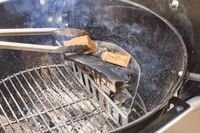 Tongs adding wood to the Weber Performer Deluxe Charcoal Grill 22-Inch