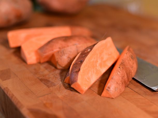 Sweet potato wedges on a cutting board, next to a chef's knife. 