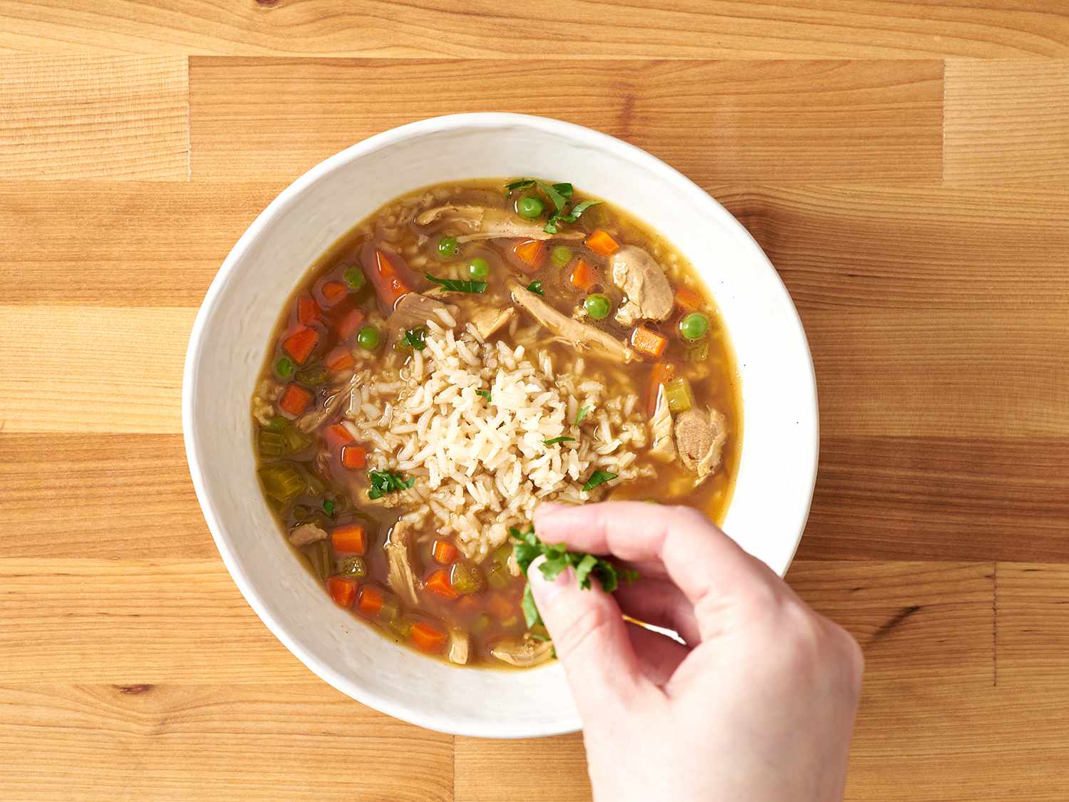 Sprinkling parsley on chicken and rice soup.