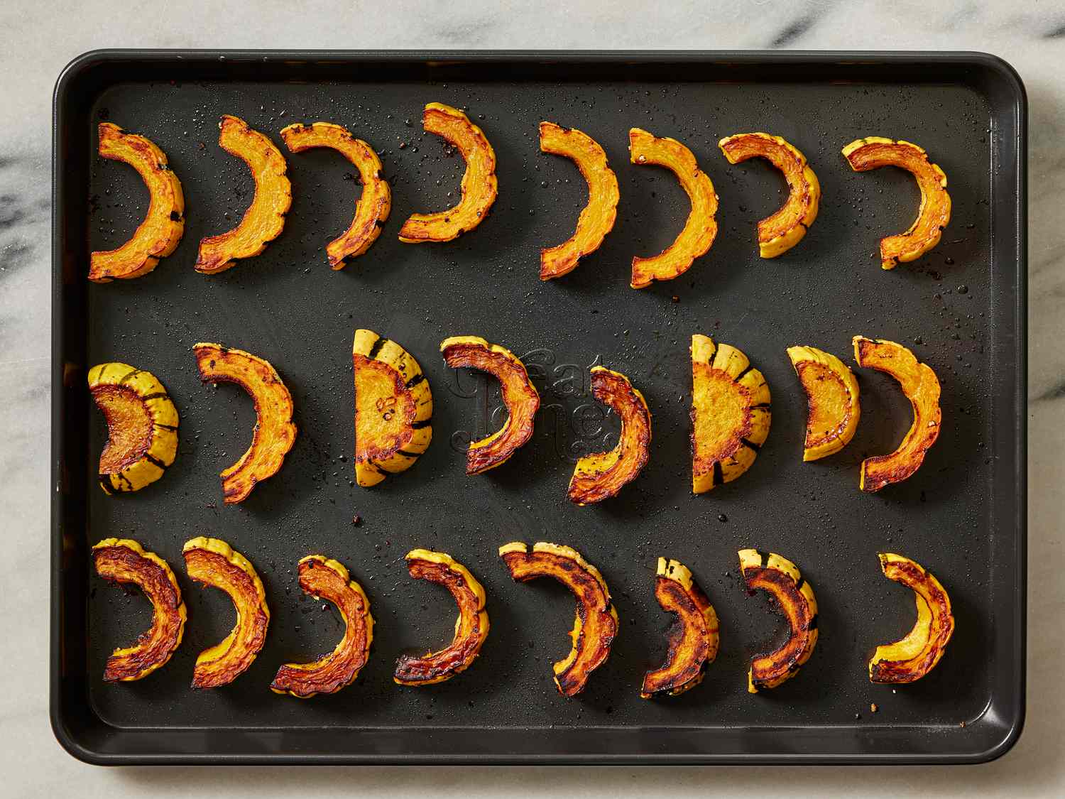 Arranged slices of squash after being roasted on a sheetpan 