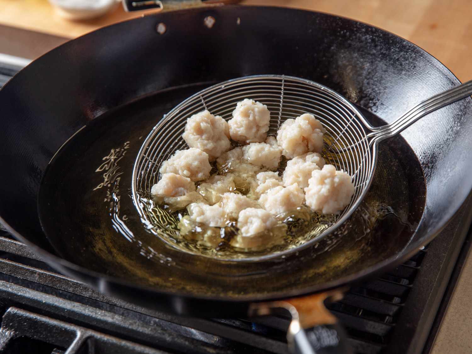 Squid balls being lowered into a wok full of oil