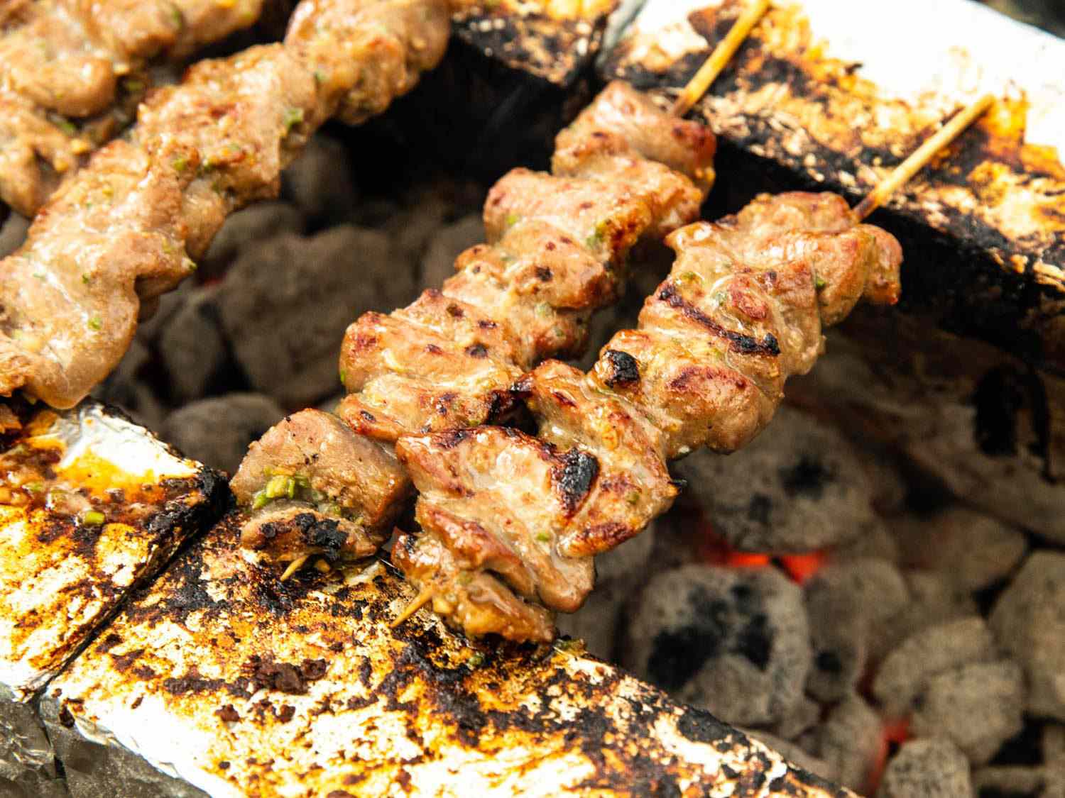 Thai pork skewers cooking directly over hot coals.