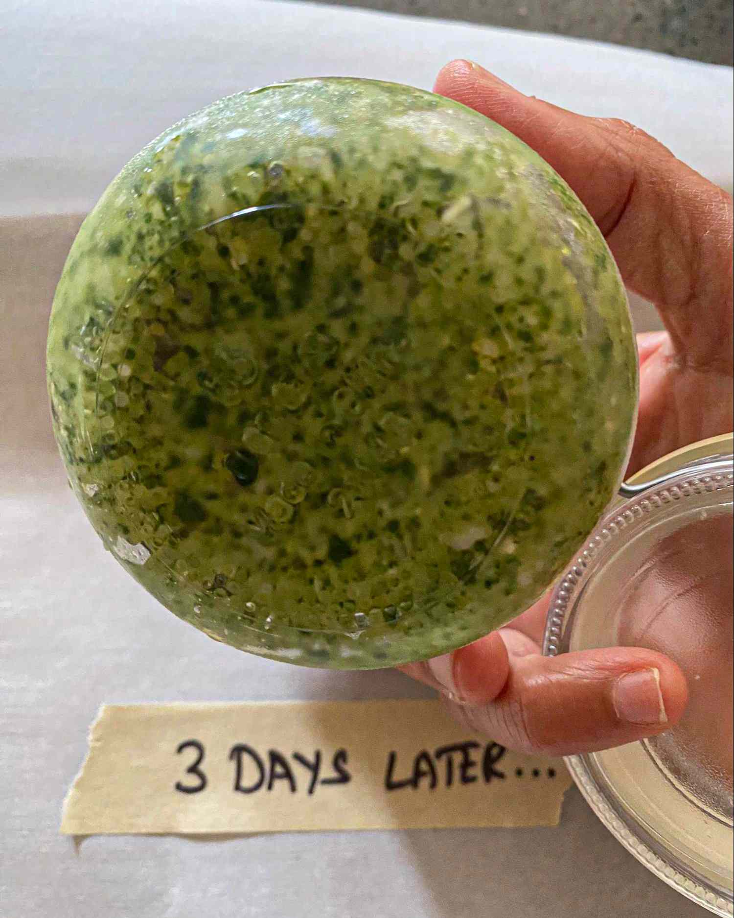 A hand holding a bowl of pesto labeled 3 days later on a slip of paper