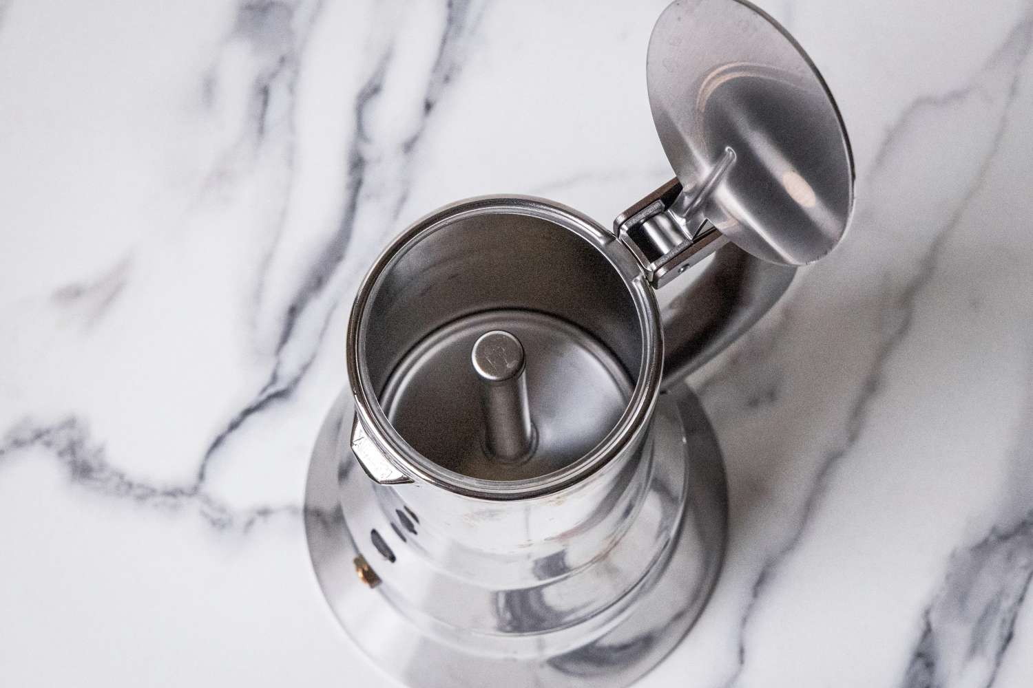 A stainless steel moka pot viewed from above with its lid open showcasing the inner components placed on a marble surface
