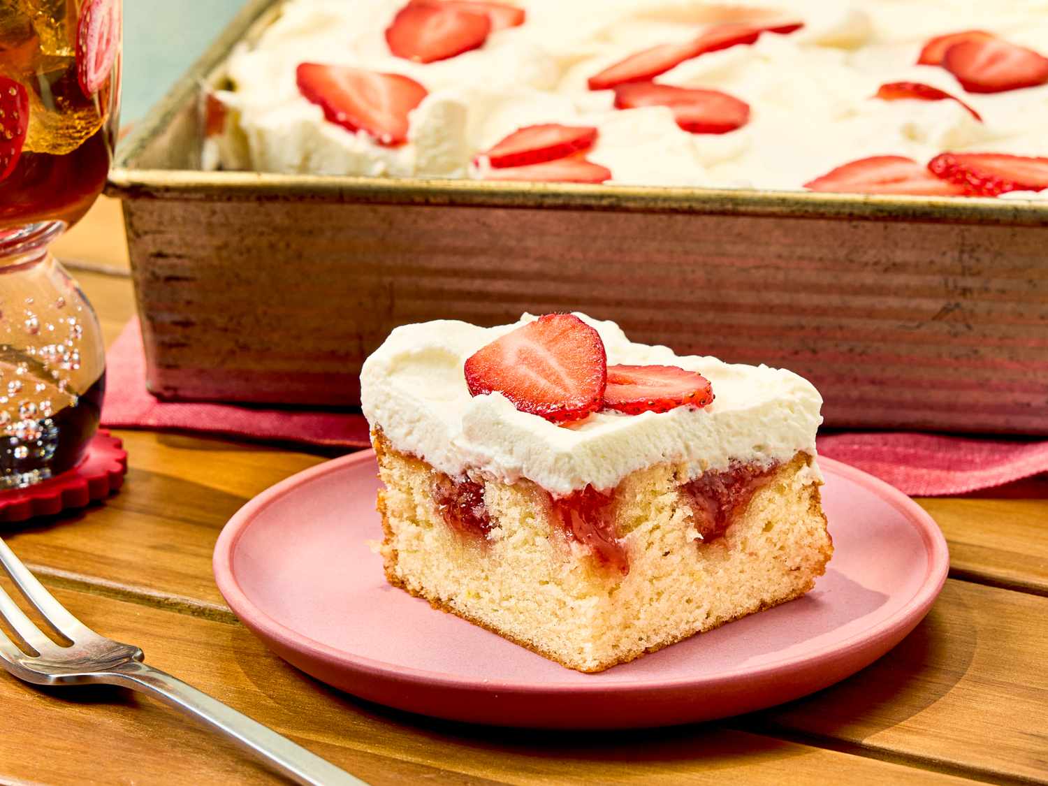 A piece of strawberry poke cake on a plate tray with more in the background