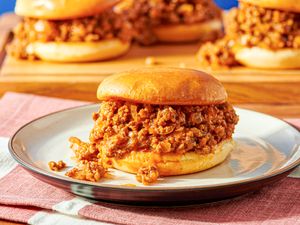 A sloppy joe served on a plate with more sandwiches in the background