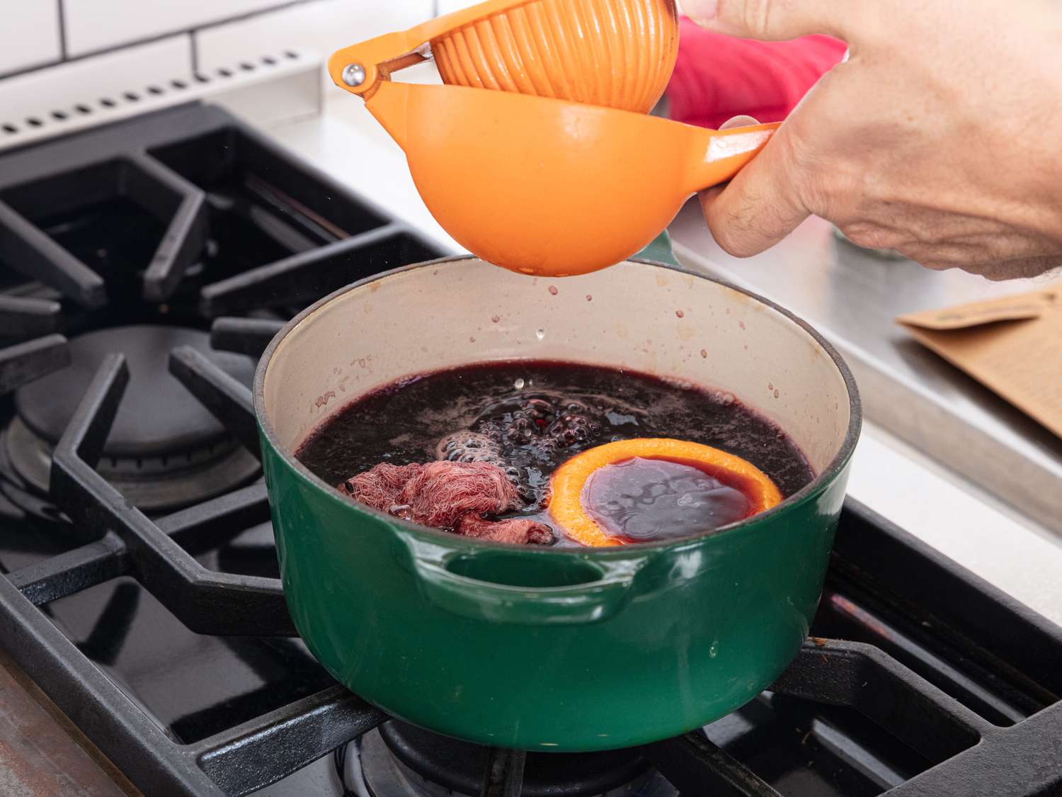 Squeezing orange juice with a squeezer into dutch oven of mulled wine on stovetop
