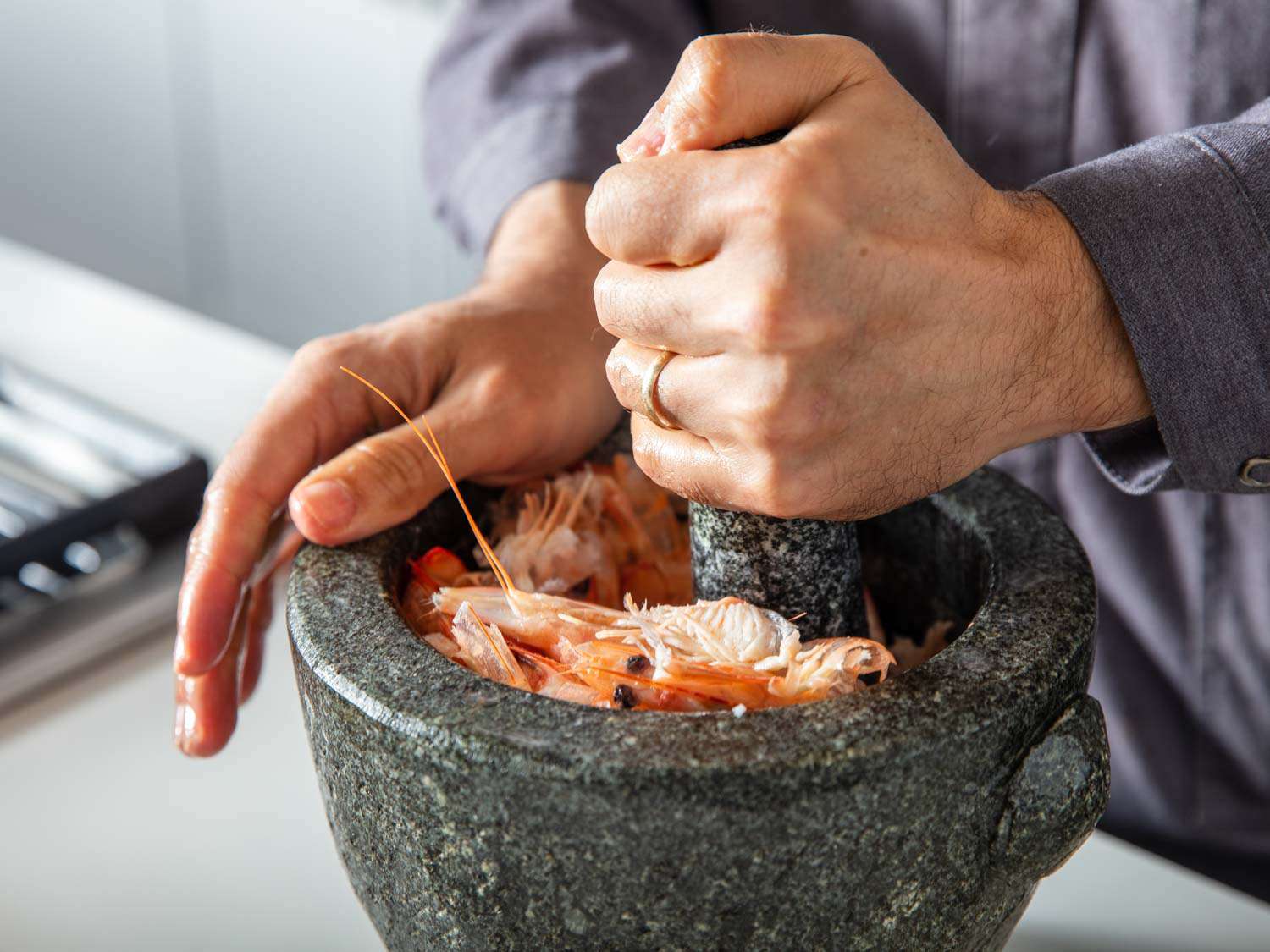 Closeup of the shrimp heads and shells being crushed with a large granite mortar and pestle.