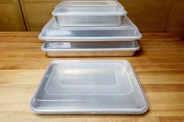 a stack of sheet pans with lids on them with one sheet pan in front