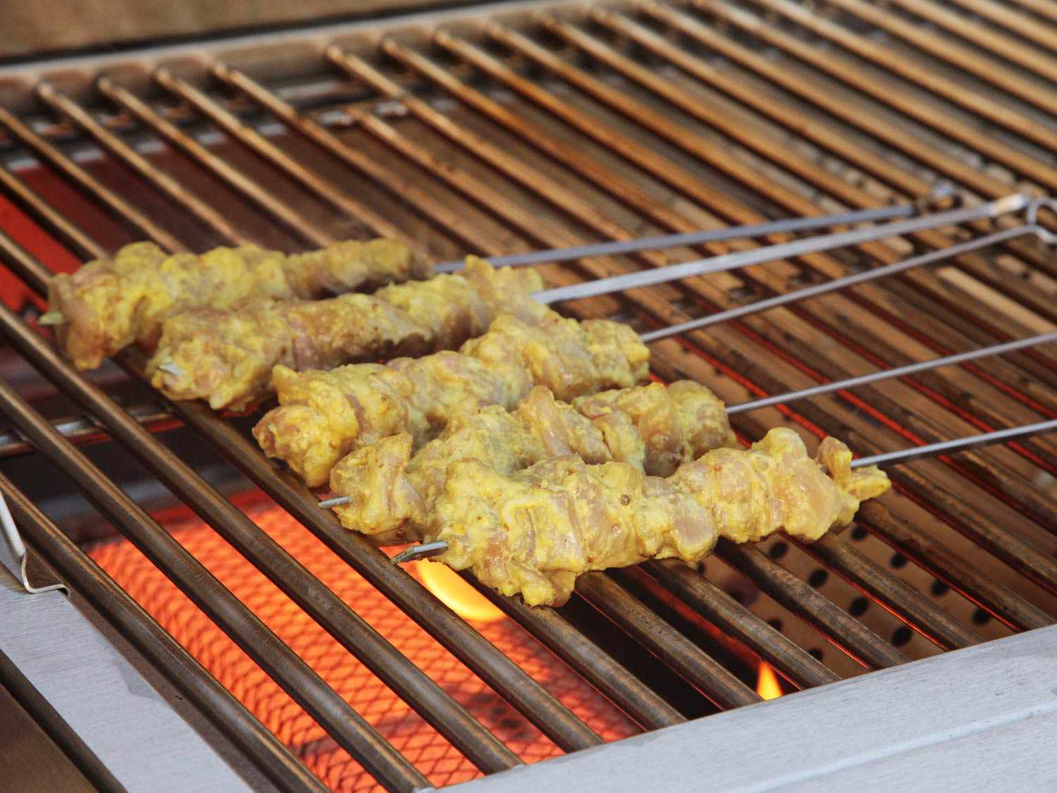 Five chicken satay skewers on a grill grate. 