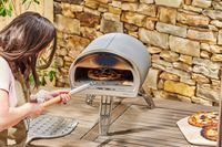 A person placing a pizza inside of the Gozney Roccbox Pizza Oven