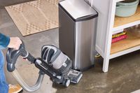 A person vacuums the area around the simplehuman 38-Liter Brushed Stainless Steel Steel Trash Can with Lid
