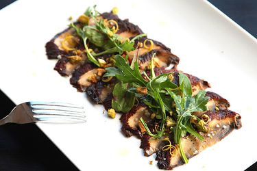 Miso-marinated portobello carpaccio served on a rectnagular white plate, garnished with chopped pistachio, lemon zest, and arugula.