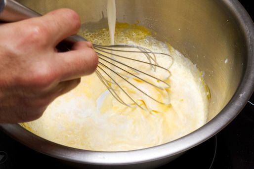 Cream being whisked into a bowl of whipped egg yolks and sugar.