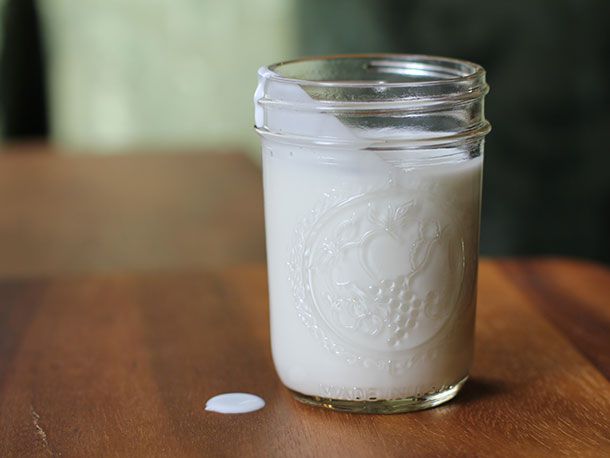 A open mason jar of DIY cultured buttermilk with a little spilled on the table.