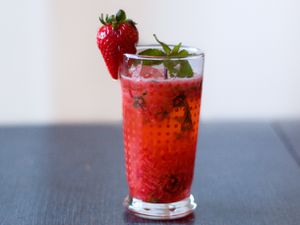 Profile view of a Strawberry Sake Cocktail, served in a tall glass with a sprig of mint and a whole strawberry gracing the rim.