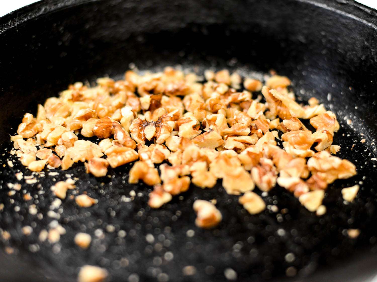Chopped walnuts toasting in cast-iron skillet.