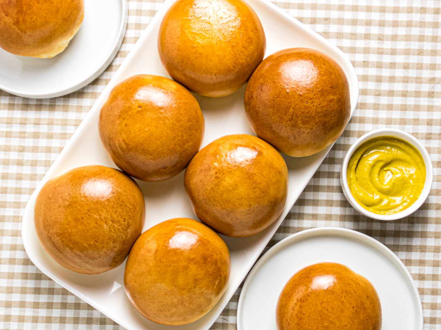 Overhead angle of 6 beirocks on a platter, with 2 plates holding a beirock on each of them on both sides of platter. Small mustard dish to the side, and a brown and white checkered tablecloth underneath.
