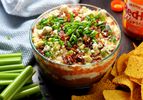 7-layer buffalo chicken dip, served in a glass bowl with tortilla chips and celery sticks.