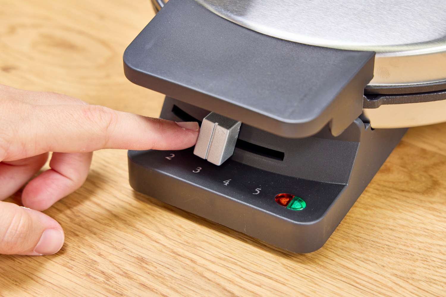 A person adjusts the slider on the front of the Cuisinart WMR-CANAS Round Classic Waffle Maker