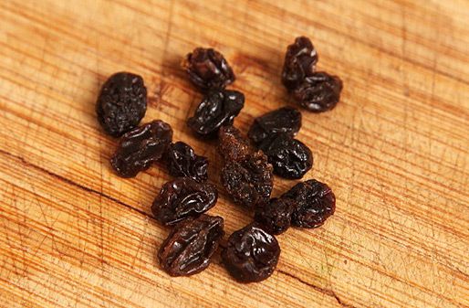 A small pile of raisins on a wood cutting board. 