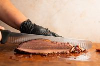 A person slicing meat using the Victorinox Fibrox Pro Slicing Knife
