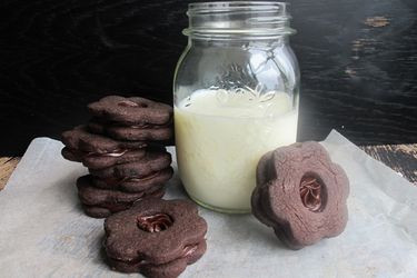 Chocolate shortbread sandwich cookies arranged around a pint-size canning jar of milk.