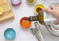 a person pouring olive oil into an orange pinch bowl