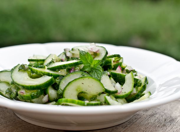 Cucumber mint salad on a white plate with out of focus outdoor greenery in background.