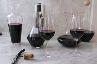 A collection of wine decanters filled with red wine on a marble counter