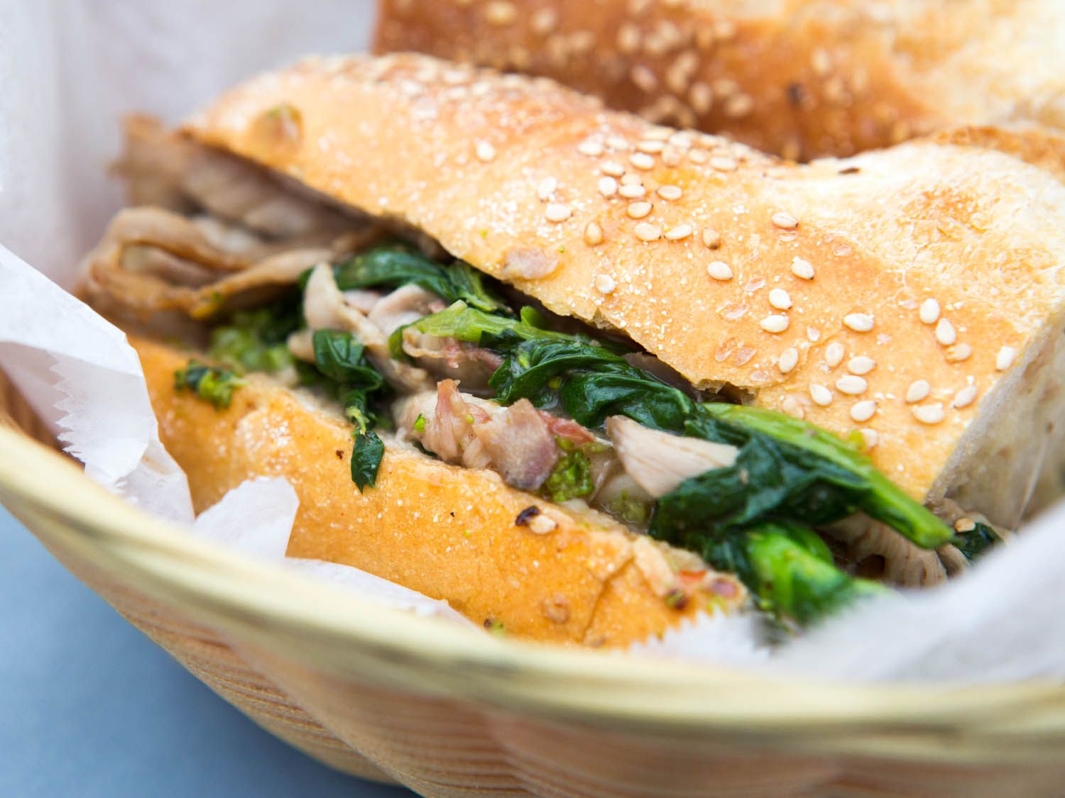 A roast pork sandwich in a basket with deli paper. 