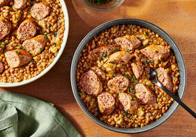 2 bowls of pressure cooked lentils and sausage on a wooden tabletop, with a soft turquoise napkin, and small bowl of parsley for garnish to the sides. 