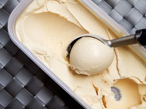 Peanut butter honey ice cream being scooped from a storage container.