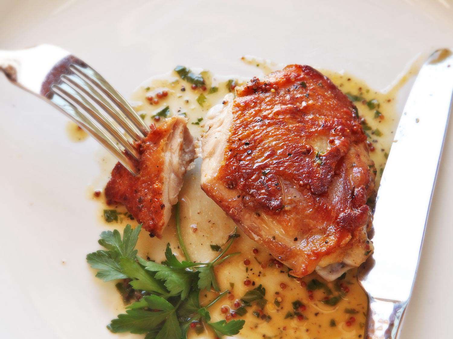 Crispy sous vide chicken thigh on a white plate with mustard pan sauce.