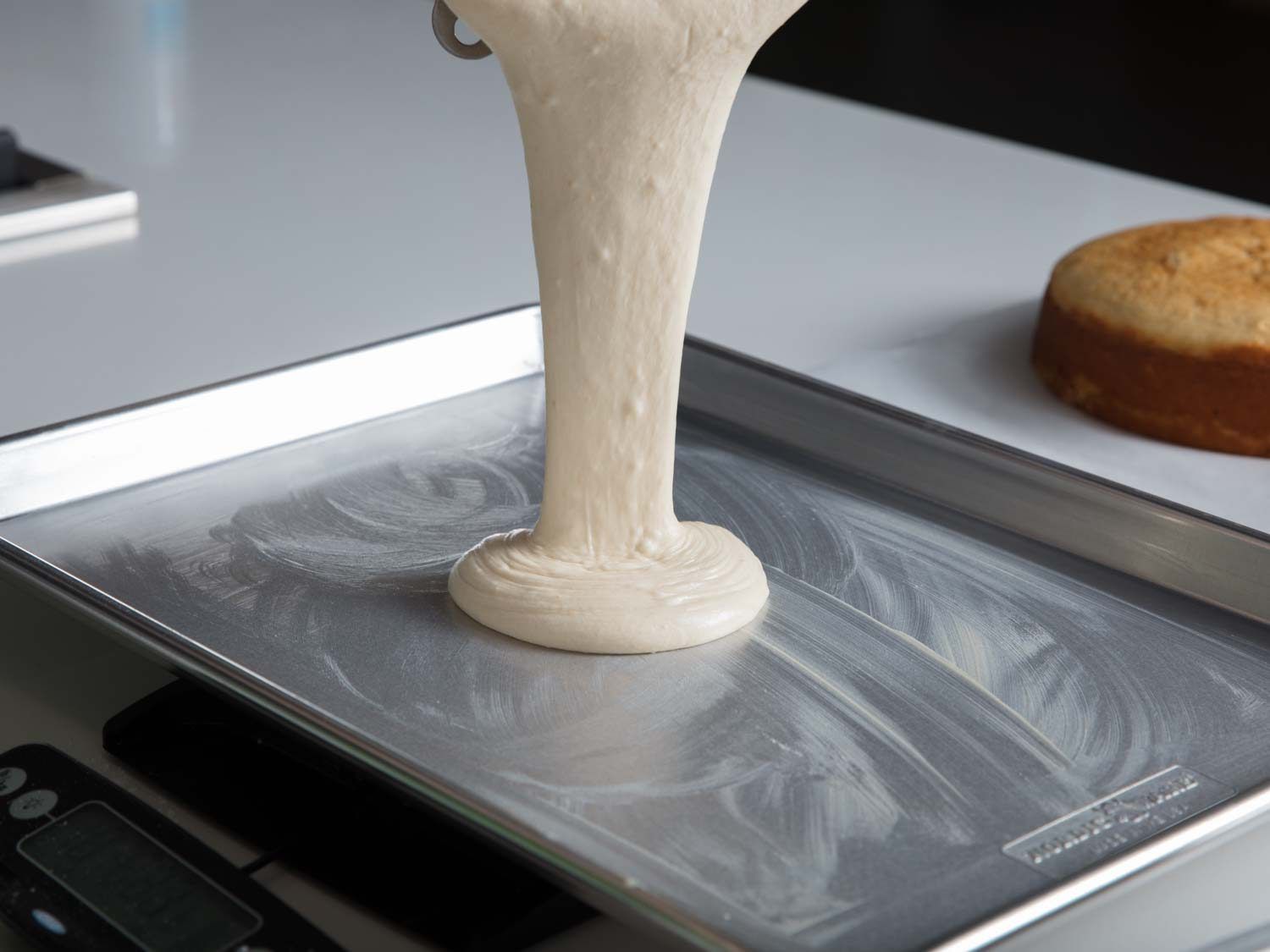 Pouring vanilla cake batter into a greased rimmed baking sheet.