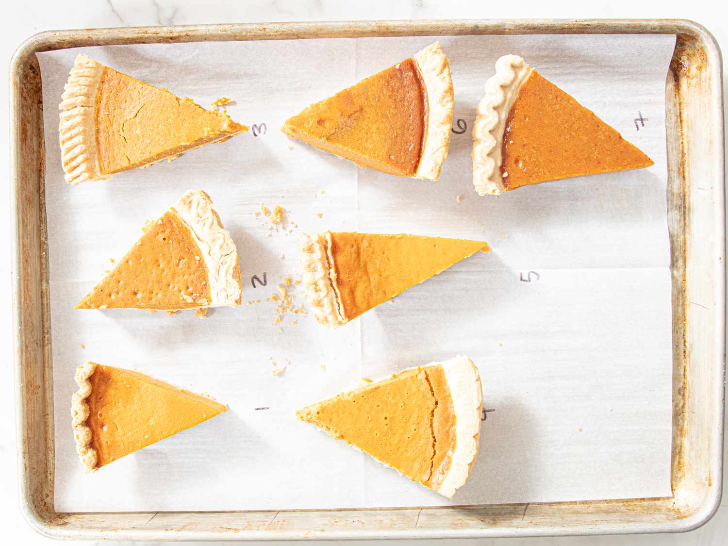 Seven slices of pumpkin pie on a baking sheet numbered 1 through 7 for a taste test or comparison
