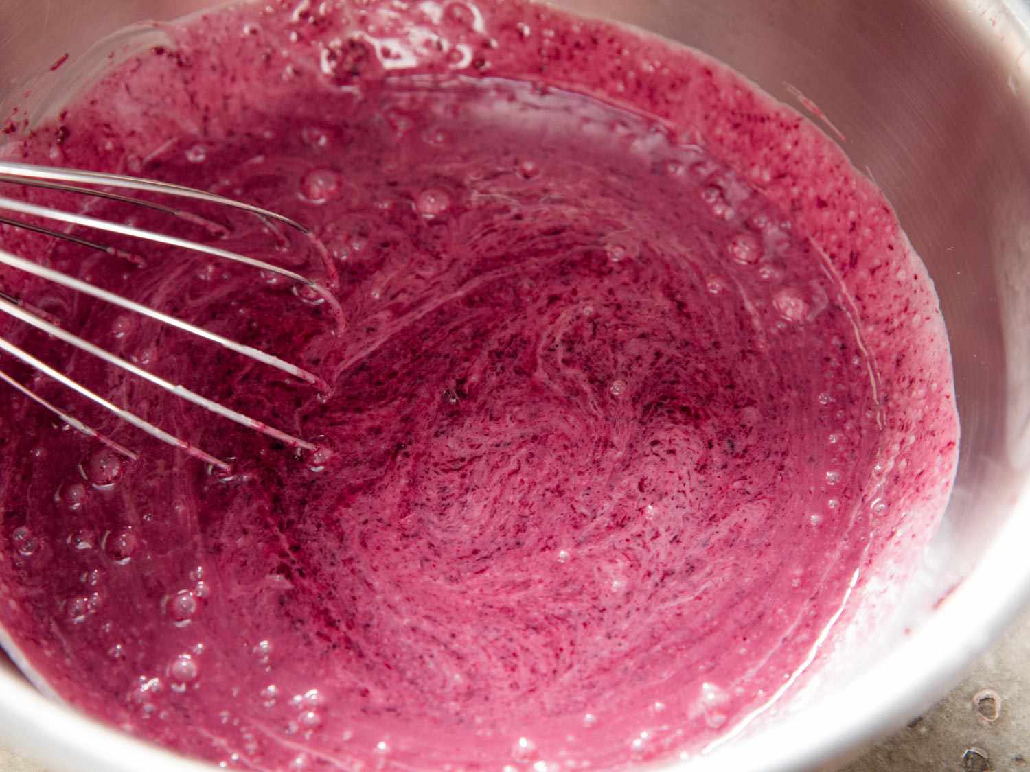 Whisking cream and cherry juice in a mixing bowl. 