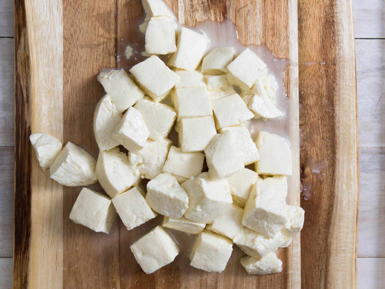 Fresh mozzarella curds cut into 1-inch cubes on a wooden cutting board.