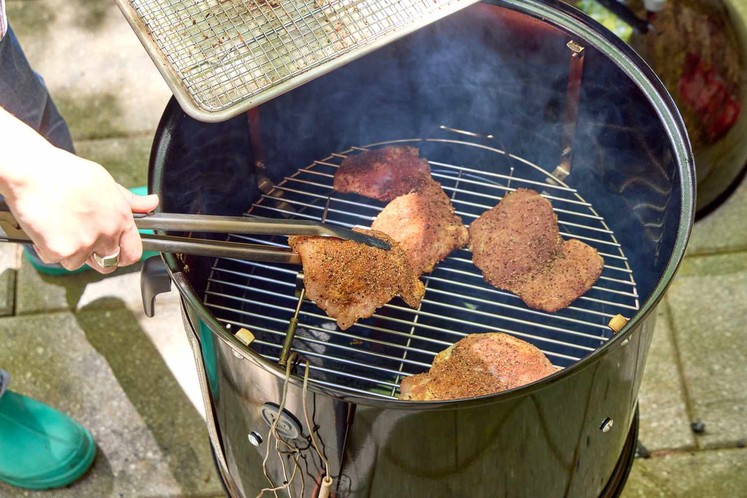 A person places meat into the Weber 18-Inch Smokey Mountain Cooker to cook