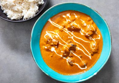 A bowl of butter chicken with a small bowl of steamed white rice next to it. 