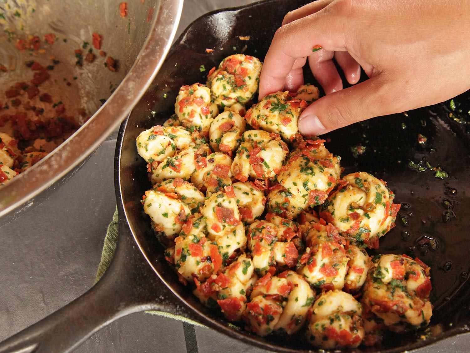 Placing pepperoni garlic knots into a cast iron pan for proofing