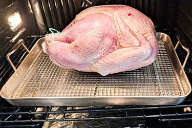 A turkey placed in an oven on a roasting pan with a rack