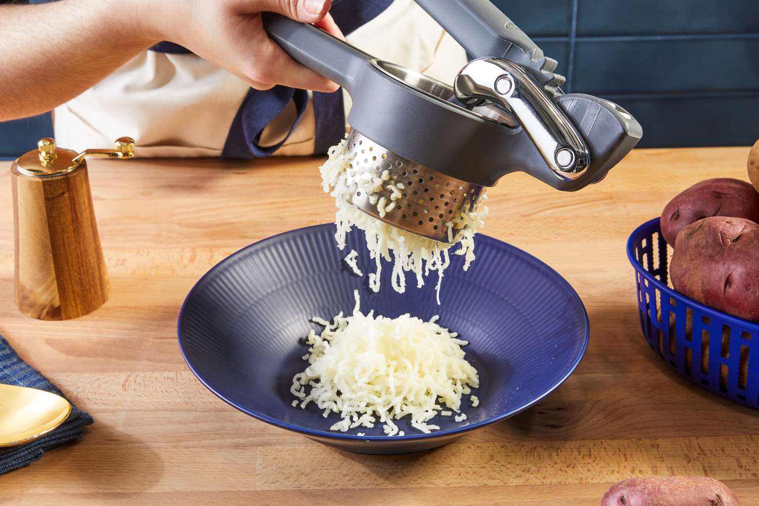 A potato ricer ricing potatoes into a blue bowl.